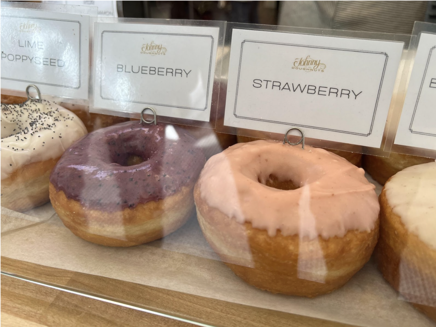Given <b>img</b>. Q: What flavor is the pink doughnut on the right? A:[sep] strawberry.. Q: What flavor is the doughnut on the left? A blueberry. 
